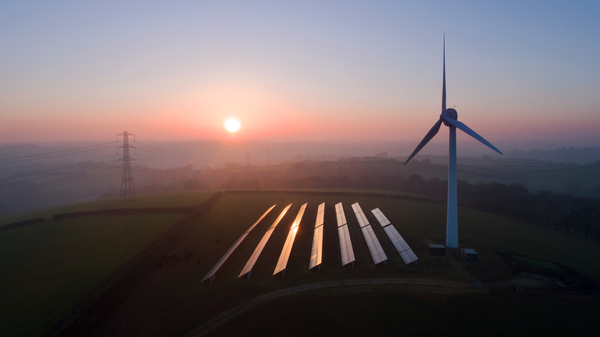 Un champ de panneaux solaires à côté d'une éolienne au coucher du soleil.