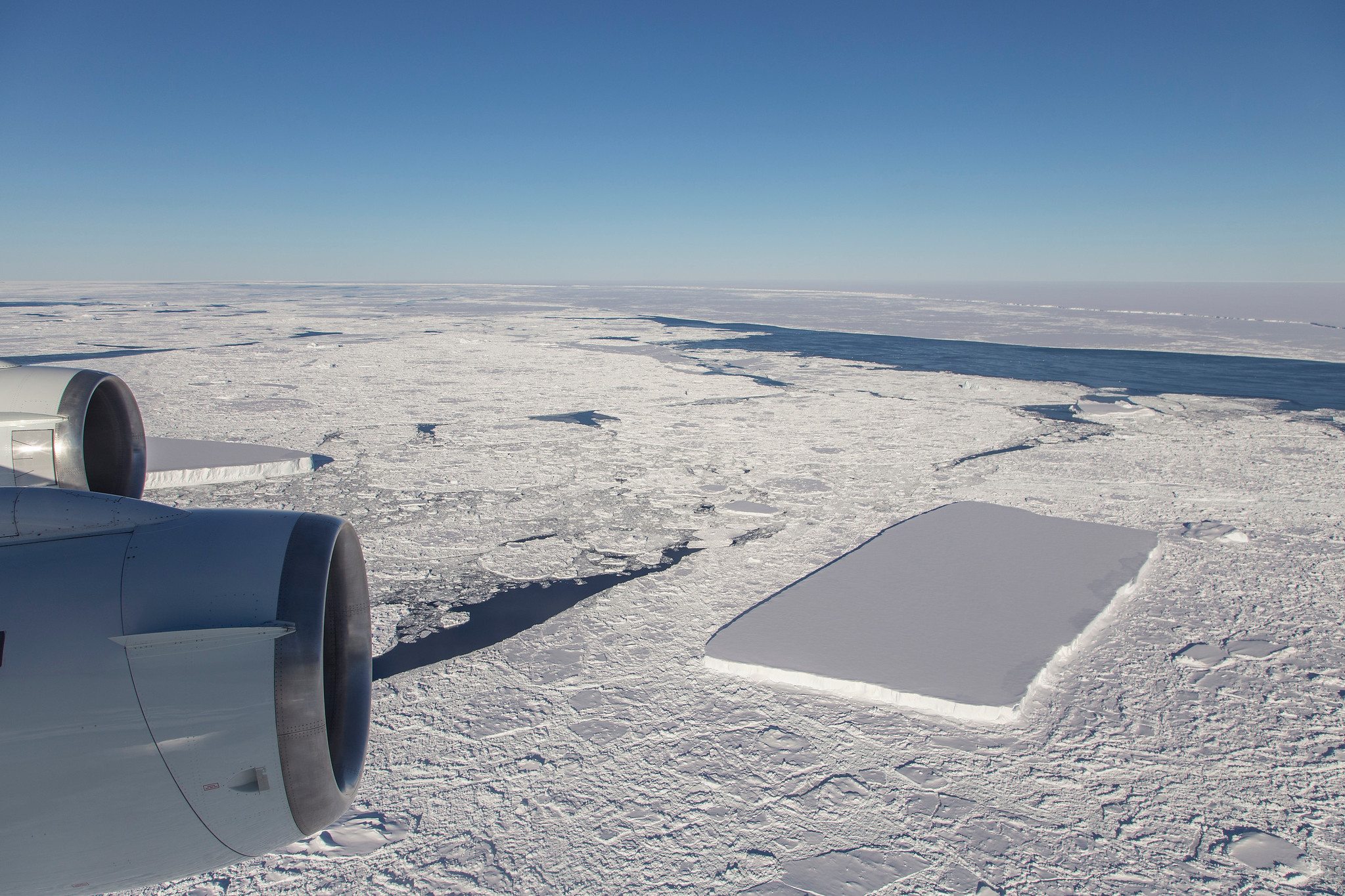 This photo, taken during an Operation IceBridge flight over the northern Antarctic Peninsula on Oct. 16, 2018, shows another relatively rectangular iceberg near the famous sharp-cornered berg, which is visible behind the plane's outboard engine. The huge, tabular iceberg A68 is visible in the distance.