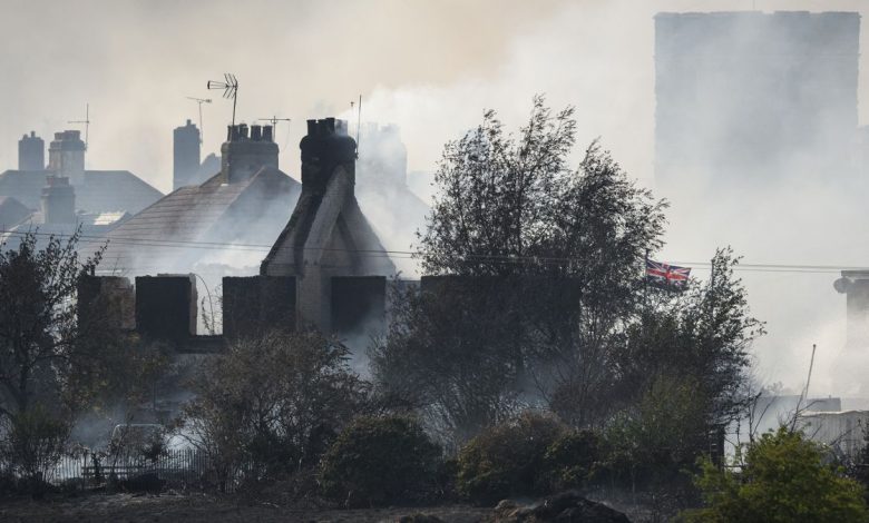 A British flag flies amongst the smoldering ruins of houses as fire services tackle a large blaze on July 19 in Wennington, England. A series of grass fires broke out amid an intense heatwave.