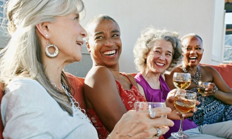 Four happy woman drinking wine together whilst sitting in a line on an urban rooftop.